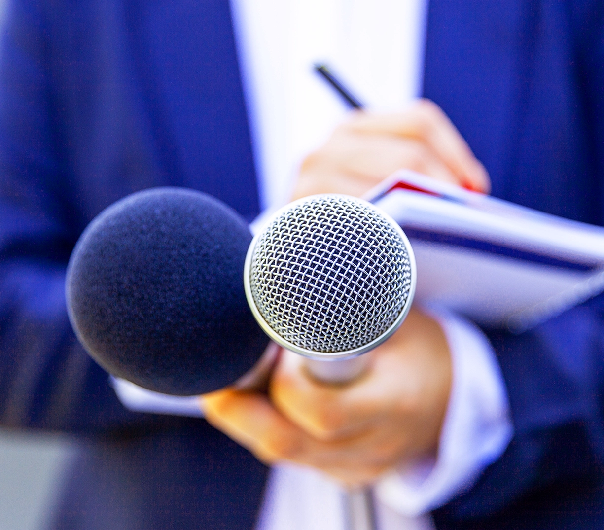 Image of a pair of microphones being held in front of a blurred person in the background.